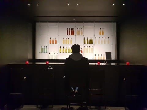 KB Kim sitting alone at a bar late at night, silhouetted against backlit bottles